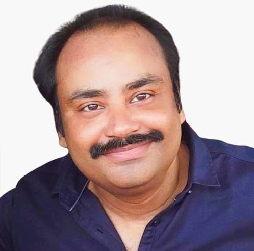 Smiling person with a mustache, wearing a dark shirt, against a plain background.